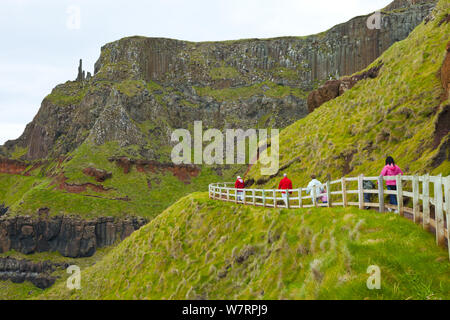 Touristen zu Fuß entlang der Küstenstraße in der Nähe des Amphitheaters, Giant's Causeway, Weltkulturerbe der UNESCO, County Antrim, Nordirland, Europa, Juni 2011 Stockfoto