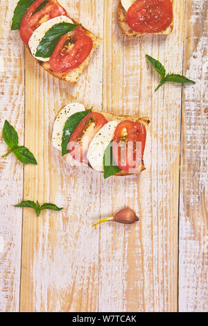 Caprese bruschetta Toasts. Bruschetta mit Tomaten, Mozzarella und Basilikum auf einem rustikalen Tisch. Traditionelle italienische Vorspeise oder Snack, Vorspeise Stockfoto