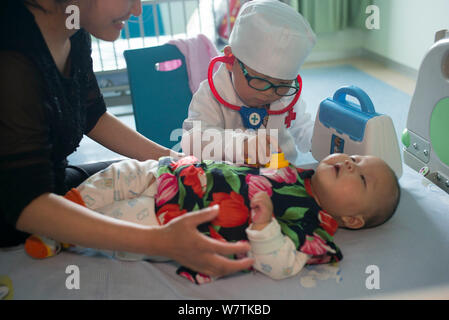 Drei-jährige Chinese Chen Chen trägt ein weißes Kleid mit einem Medical Kit wird dargestellt, wie er Checkup Patienten gibt in eine Kinderklinik in Wu Stockfoto