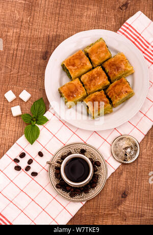 Turkish Delights: Traditionelle Baklava-Süßigkeiten mit türkischem Kaffee, Zucker und Blick von oben auf Holztisch und weißem Stoff Stockfoto