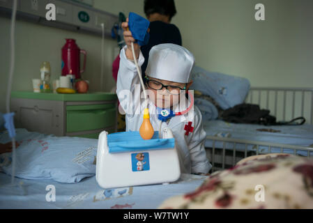 Drei-jährige Chinese Chen Chen trägt ein weißes Kleid mit einem Medical Kit wird dargestellt, wie er Checkup Patienten gibt in eine Kinderklinik in Wu Stockfoto