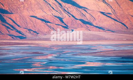 Am frühen Morgen über die Berge in der Ferne, die Schaffung pulsierenden Reflexionen in den Salinen von Death Valley National Park, Kalifornien, USA, Dezember 2013. Stockfoto