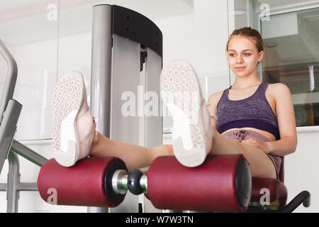 Junge schöne Blondine sportliche Mädchen entspannt nach einem Leg Extension Training in einem Fitnessstudio Stockfoto