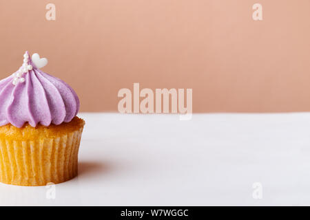 Cute Cupcake mit kleinen weißen Herzen auf lila Creme auf rosa Hintergrund Stockfoto