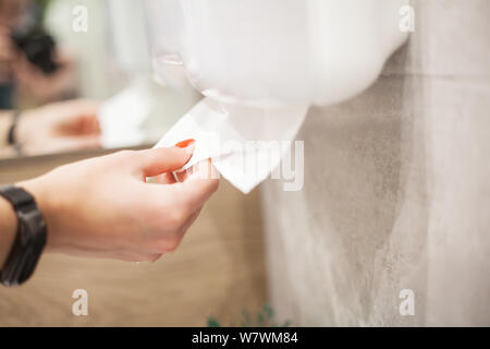 Papierhandtuchspender. Hand der Frau nimmt Papier Handtuch im Bad. Stockfoto
