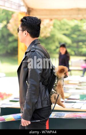 Ein chinesischer Mann verwendet einen "baby Sling' seinen Hund zu unterstützen, während er während einer Buchmesse in Huaian Stadt hängt in der ostchinesischen Provinz Jiangsu, 23. April Stockfoto