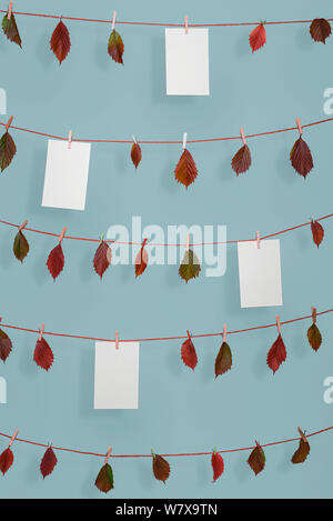 Herbst Hintergrund mit bunten Laub hängenden auf Zeichenketten und leeren White Papers, mit Holz- klemmen, auf blauen Wand. Herbst Rahmen mit kopieren. Stockfoto