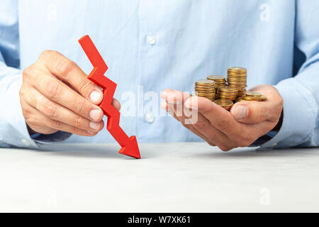 Mann im blauen Hemd hält einen nach unten zeigenden Pfeil und Münzen in der Hand. Konzept der sinkende Gewinne oder Geschäft Bankrott Stockfoto