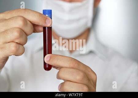 Reagenzglas in männlicher Hand Nahaufnahme, Mann in der medizinischen Maske eine Durchstechflasche mit roter Flüssigkeit. Konzept der Blutprobe, medizinische Forschung, Impfung Stockfoto
