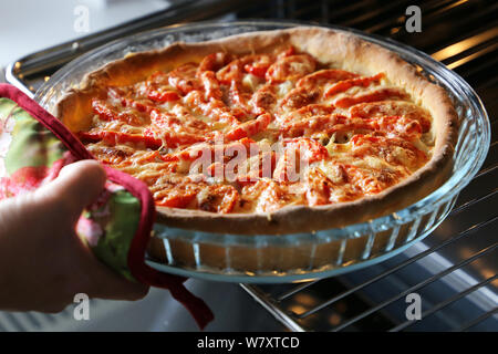 Pizza Kochen, Frau nimmt die frisch gebackene Kuchen mit Käse, Fleisch und Tomaten aus dem Ofen Stockfoto