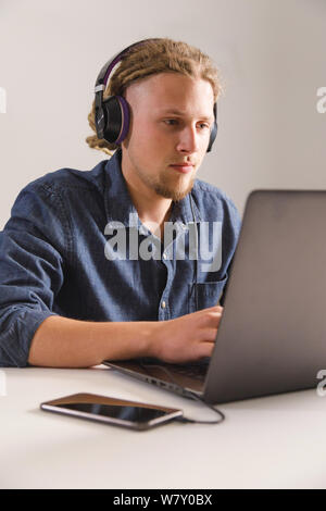 Ernst selbstbewussten jungen Freelancer in legere Kleidung arbeiten und konzentrierte sich auf Laptop beim Sitzen am Schreibtisch in der modernen Flachbild Stockfoto