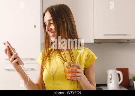 Bild der brünette Mädchen, dass Smartphone und Glas Saft am Morgen in der Küche Stockfoto