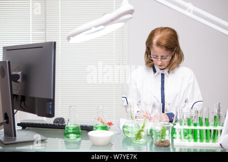 Frau mittleren Alters, die sich Notizen nach wissenschaftlichen Tests in einer Produktion Labor konzentriert. Der Biologe arbeitet. Stockfoto