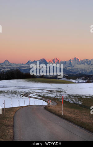 Weg durch Winterhügel auf dem Gurten mit buntem Abendhimmel und berühmten jungfrau-Gebirgszug Eiger, Mönch und Jungfrau. Stockfoto