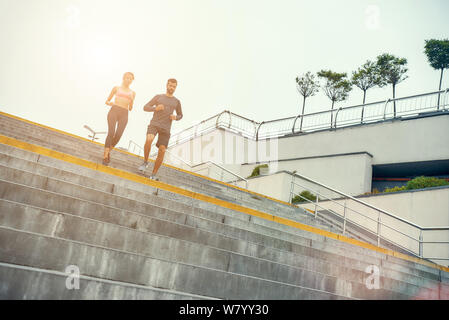 Gehen Sie in voller Länge von jungen Paar in Sportbekleidung läuft die Treppe hinunter, während Sie im Freien trainieren. Sportkonzept. Gesunder Lebensstil Stockfoto
