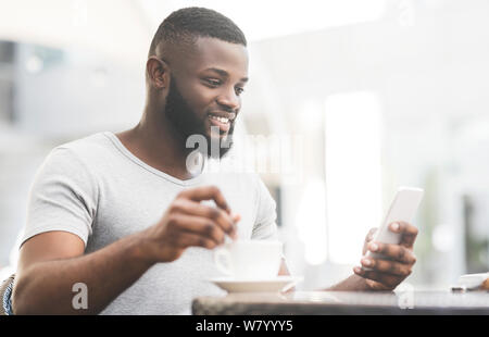 Bärtige afrikanischen Mann mit Tasse Kaffee lesen am Handy Stockfoto