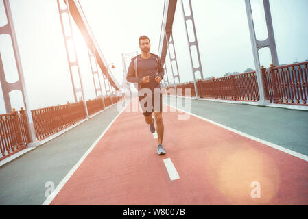 Nie aufgeben volle Länge der jungen und schönen bärtigen Mann in Sportkleidung Joggen auf der Brücke am Morgen. Sportkonzept. Gesunder Lebensstil. Sport Stockfoto