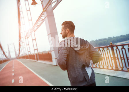 Tägliche Routine. Rückansicht des jungen gutaussehenden Mannes in Sportkleidung Joggen auf der Brücke am Morgen. Sportkonzept. Gesunder Lebensstil. Wellness-Konzept Stockfoto