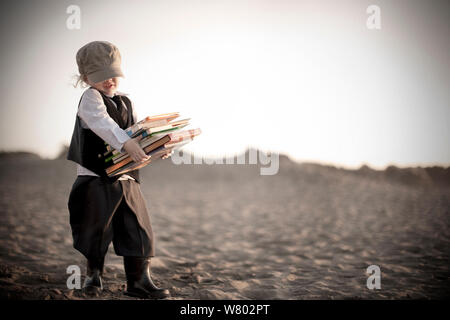 Kleiner Junge, der in der viktorianischen Ära Kleidung tragen Bücher Strand entlang Stockfoto