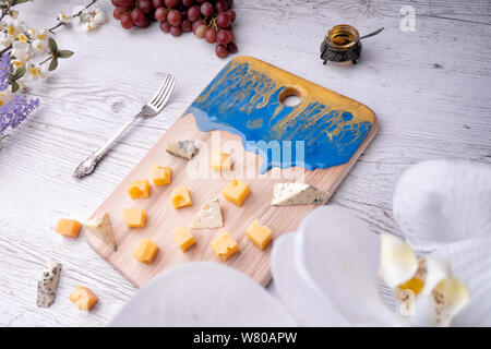 Zusammensetzung Schneidbrett mit einer abstrakten Muster, Käse, Honig, Trauben, Orchidee Blumen, auf hellem Holz der Tischplatte. Stockfoto