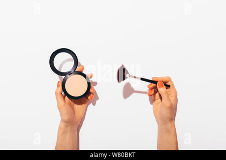 Weibliche Hände halten gepressten Puder und Make-up-Pinsel auf weißem Hintergrund, flach Konzept Komposition mit hartem Licht. Stockfoto