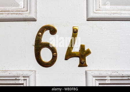 Haus Nummer 64 in Bronze Metall Ziffern auf weißem Holz- Vordertür Stockfoto