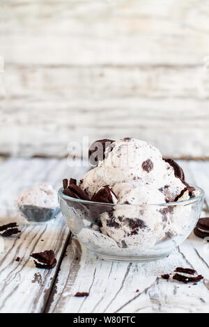 Klares Glas Schale mit Cookies und Sahne Eis. Selektiver Fokus mit unscharfem Hintergrund. Ganze und zerbröckelt Creme gefüllt Cookies über Tabl verstreut Stockfoto
