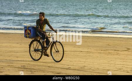 Ein Verkäufer Radfahren am Strand in Goa sieht für Kunden Stockfoto
