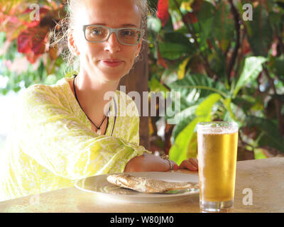 Eine Frau lächelt sitzen in einer Bar mit Bier und getrockneten Fisch. Stockfoto