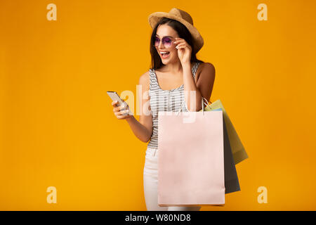 Mädchen mit Handy Holding bunten Einkaufstaschen auf gelbem Hintergrund Stockfoto