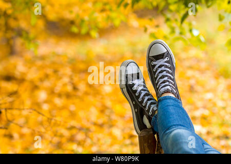 Entspannt Jugendmädchen Sneakers tragen liegt auf der Werkbank im Herbst park Nahaufnahme. Fokus auf Turnschuhe. Stockfoto