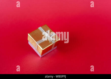 Weihnachten goldenen Geschenkkarton mit einer Band mit einem Bogen auf einem roten Hintergrund mit einem Platz für die Beschriftung gebunden. Stockfoto