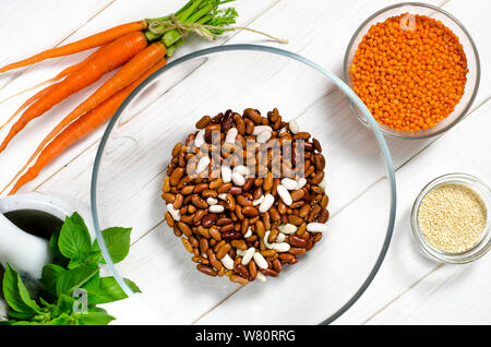 Die Bohne Diät. Bohnen, Linsen, Sesam, Knoblauch und Basilikum in Glasplatten stehen auf einem weißen Tisch Stockfoto