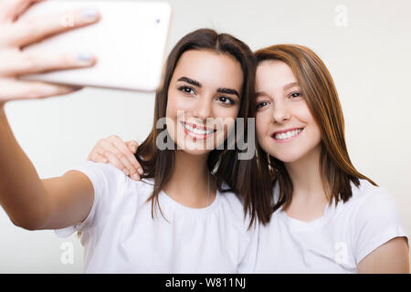 Zwei schöne junge Frau in Weiß eine selfie lächelnd und umarmt auf einem weißen studio Hintergrund isoliert gekleidet. Stockfoto