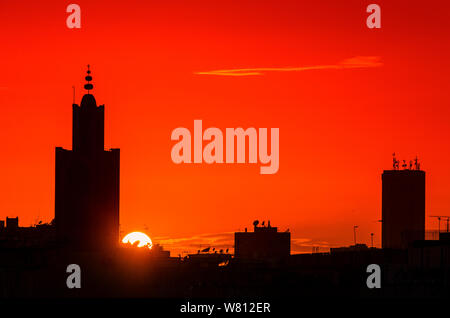 Sonnenuntergang über der Stadt, eine Moschee und Gebäude in Silhouette auf einem Hintergrund von Orange Sky. Stockfoto