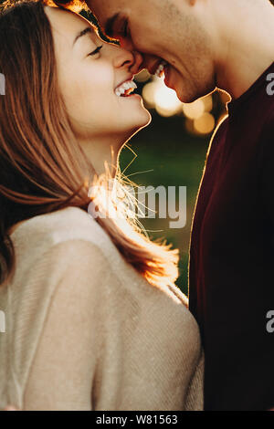 Close up Portrait von schönen kaukasischen Paar eng lachend vor dem Küssen mit geschlossenen Augen gegen Sonnenuntergang unterwegs. Stockfoto