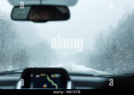 Ein Blick auf den winterlichen Wald und Berge mit Schnee von der Windschutzscheibe des Autos. Es ist ein Navigationssystem im Auto und ein Schnee, Nebel und oben Stockfoto