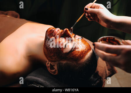 Porträt einer schönen jungen Frau lehnte sich auf ein Bett mit geschlossenen Augen, während mit einer Schokolade Maske in einem Wellness Resort unterwegs. Stockfoto