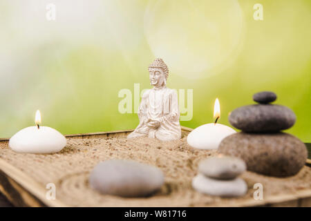 Miniatur Schreibtisch zen Sandbox mit Buddha Figur sitzen im Lotussitz, gestapelte zen Meer Steine, Wellness Kerzen brennen gegen grüne Bokeh studio Hintergrund Stockfoto