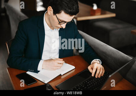 Bild von einem kaukasischen Geschäftsmanns, der während des Betriebs einen Laptop und Notizen. Stockfoto