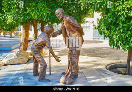 SHIRAZ, IRAN - Oktober 14, 2017: Der bronzene Denkmal, die alten Großvater und seinem Enkel, und half ihm, die Koffer zu tragen, am 14. Oktober in Stockfoto