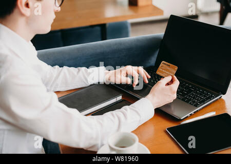 Seitenansicht eines jungen kaukasischen Hand tun Online Transaktion mit einem Gold Kreditkarte und einem Laptop, während in einem Café sitzen. Stockfoto