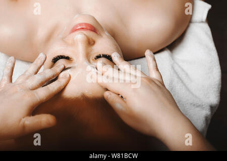 Nahaufnahme, Porträt einer schönen Frau, Anti age Gesichtsmassage mit Schaum durch eine weibliche Kosmetiker in einem Wellness Spa Resort. Stockfoto
