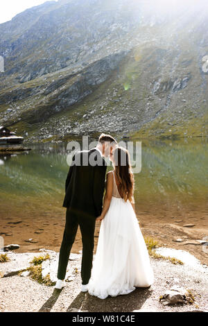 Die volle Länge einer erstaunlichen Bräutigam und Braut am Rande eines Sees in den Bergen zu küssen. Stockfoto