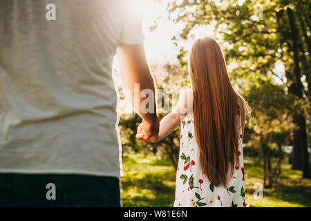 Rückansicht eines roten Haare Mädchen führenden seinen Freund seine Hand gegen Sonnenlicht gehen in den Park. Stockfoto