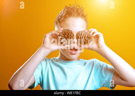 Ein Junge in einem hellen T-Shirt setzen zwei Kegel seine Augen auf einem hellen farbigen Hintergrund Stockfoto