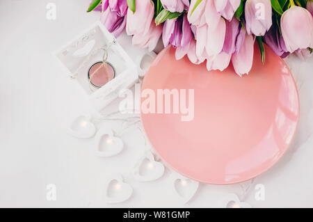 Rosa Teller mit einer Girlande in Herzform auf hellem Hintergrund. Flache Position, Draufsicht, Kopierbereich. Stockfoto