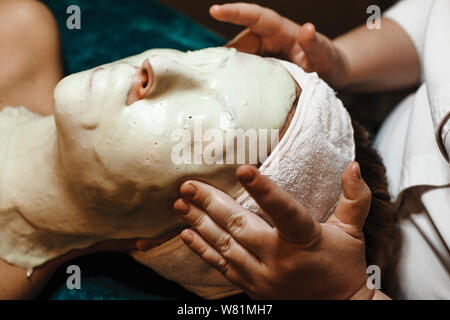 Seitenansicht Nahaufnahme eines womans Gesicht lehnte sich auf ein Spa Bett voll von bio Alginat Maske abgedeckt. Kosmetiker Ihr Kopf ist zu massieren. Stockfoto