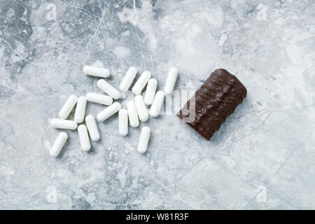 High Protein Bar und Arginin kapseln. Bodybuilding Nahrungsergänzungen auf hellen Stein Hintergrund. Ansicht von oben. Kopieren Sie Platz. Stockfoto