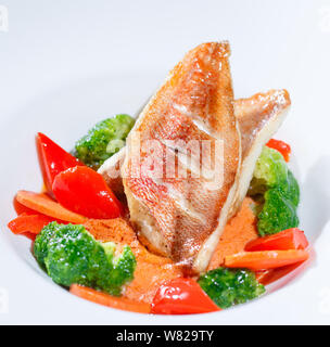 Fisch mit Gemüse auf einem weißen Teller auf dem Hintergrund einer hölzernen Tisch. Stockfoto